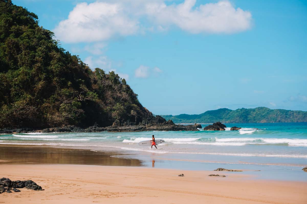 Duli beach with mountains in background and surfer walking out of the sea